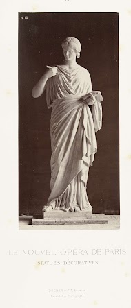 Marmeren beeld van een vrouw in toga met in haar handen een papier en een pen.