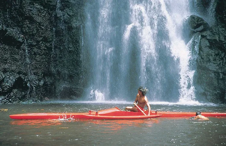A Tahitian man kayaks near a waterfall on Tahiti. Visitors are encouraged to do the same. 