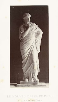 Marmeren beeld van een vrouw in hooggesloten gewaad, ze heeft een vinger opgeheven.