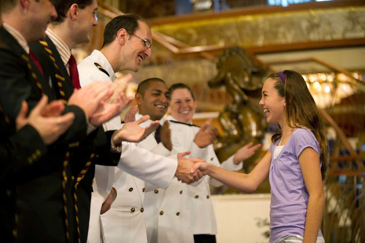 Crew members greet a young guest on Disney Dream.  
