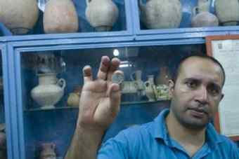 ak Samer holds a 2,000-year-old coin in his shop in Jerusalem. Coins like this are commonly robbed from archaeological sites in Israel. 
