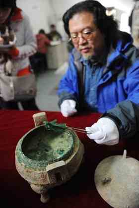 Liu Daiyun, a Shaanxi Provincial Archeological Institute official, shows a piece of bone in a recently discovered bronze vessel in Xi'an, northwest China's Shaanxi Province, Dec. 10, 2010. A 2,400-year old bronze vessel containing soup with bones has been discovered recently in a tomb excavated in Xi'an. The vessel is 20 centimeters tall and has a 24.5 centimeters diameter. The archeologists also unearthed a bronze pot containing an odorless liquid, which may be ancient wine. 