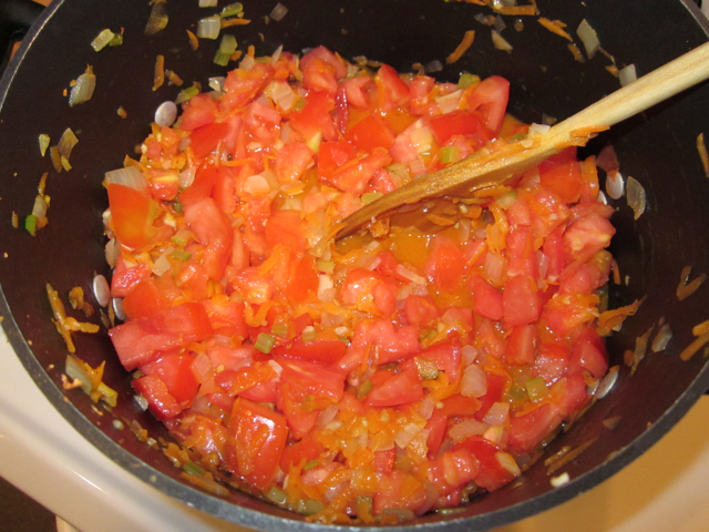 Tomatoes added to other veggies in pot and stirred with wooden spoon 