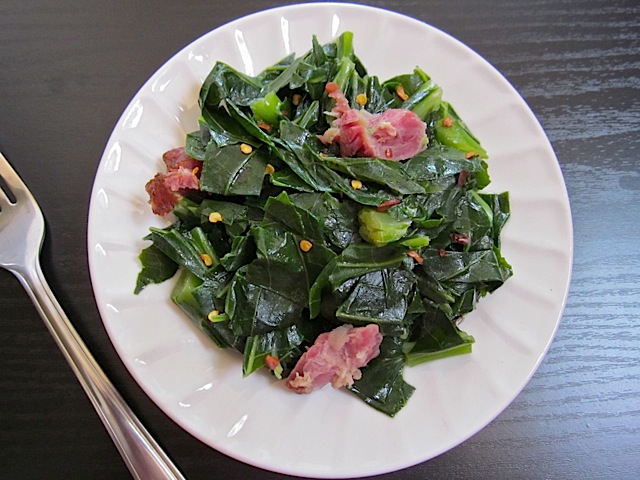 collard greens and ham hock plated on white plate with fork on side 