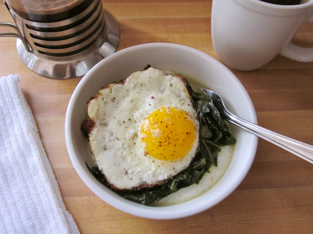 Grits, greens and fried egg in white bowl with fork, ready to eat 