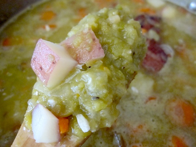 mushy peas in simmered soup, being held up close to the camera on a wooden spoon