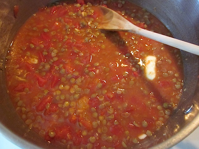 tomatoes added to lentils and spices in pot with wooden spoon 