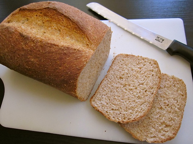 honey wheat sandwich bread with two slices being sliced on cutting board with knife