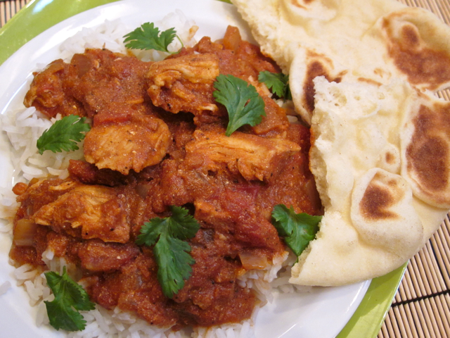 not butter chicken on pile of jasmine rice plated on white plate with a side of naan. 