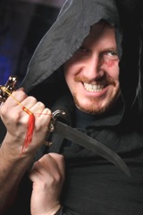 medieval looking menacng man with dagger wearing black cloak with hood