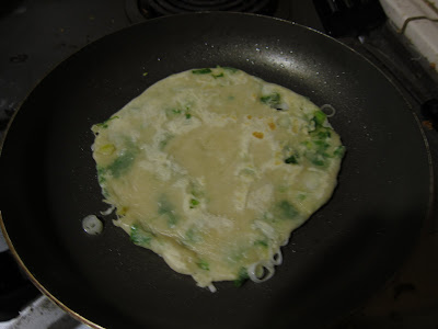 photo of a green onion pancake cooking in a pan