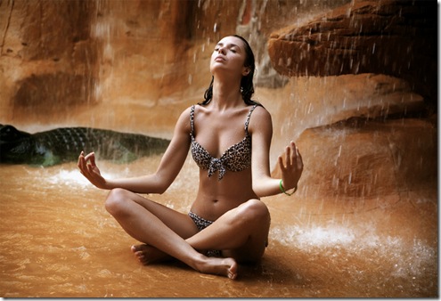 Young woman doing yoga exercise under waterfall