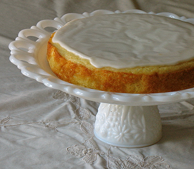 A close up photo of a lemon cornmeal cake on a white cake stand.