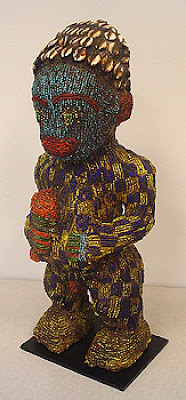 Royal Male Ancestral Figure- small of carved wood covered with indigenous royal fabric & glass seed bead male figure standing holding drinking horn in right hand, head adorned with cowrie shells, turquoise blue face, blue & yellow checkerboard pattern covers body. 20th century.  16.75" h x 6.50" w x 5.50"d, mounted.