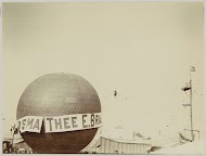 Luchtballon met reclame voor 'Thee E. Brandsma', op de achtergrond een koorddanser boven een kermisterrein