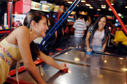 Quarter-Masters-Disney-Magic-and-Wonder - Girls play a game of air hockey at Quarter Masters, the young people's arcade on deck 9 at midship of Disney Magic and the Disney Wonder next to Quiet Cove Pool. The arcade also features tons of videogames.