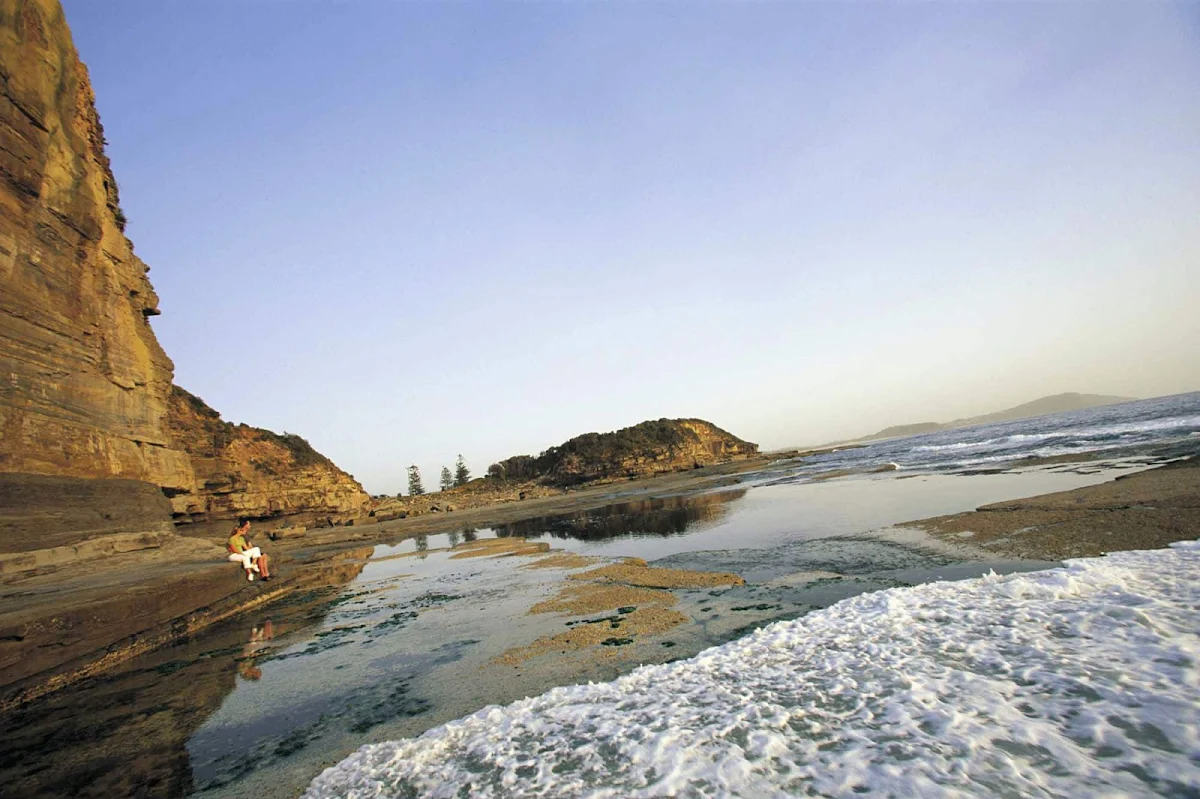 Skillion-coastline - A couple sits on a rock ledge taking in The Skillion, Terrigal, along Australia's Central Coast NSW.