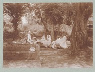 Een gedekte tafel in de tropen met daaraan Europese mensen gekleed in het wit.