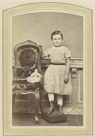 Portret van een meisje in een gestreepte jurk met een pop bij een stoel