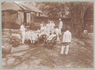 Europeanen gekleed in het wit ontspannen bij de buitentafel terwijl de Indonesische bediende het van een afstand gade slaat.