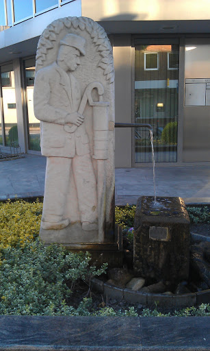 Stein-Skulptur Mann an einer Wasserpumpe