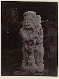 Beeld van een tempelwachter met in zijn hand een slag instrument bij Candi Panataran.